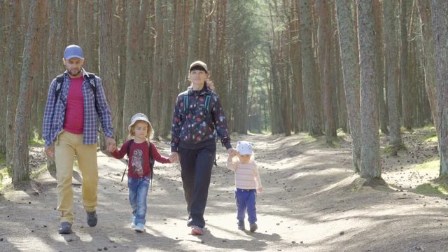 Sports family travels through  forest. A young mother of a tourist with a backpack leading her children through a forest road. Family travel together, hiking outdoors on nature.