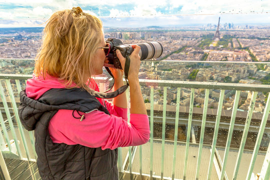 Travel woman photographer with telelens takes photos of Eiffel Tower from panoramic terrace of Tour Montparnasse. Female photographer in French capital, Europe.Paris skyline.Popular travel destination