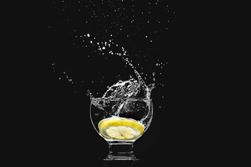 Splash in a glass of pure water with a lemon isolated on a black background - obrazy, fototapety, plakaty