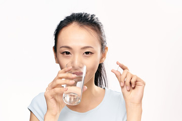Beautiful young woman on white isolated background, drink pill, asian