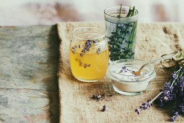 Organic raw honey, white sugar in glass jars, glass of water flavored with lavender flowers, standing on table with sackcloth. Rustic style, day light