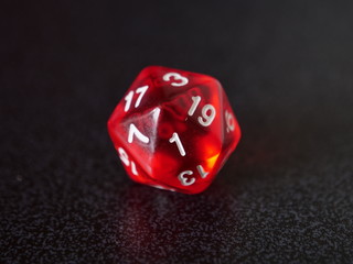 Close up on red transparent 20 sided gaming die, known as a d20, showing a 1 which is significant...