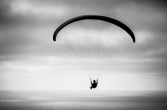 Hang glider flying over the ocean against the sky; black and white image 