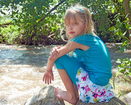 young Caucasian girl sitting on a rock by river edge