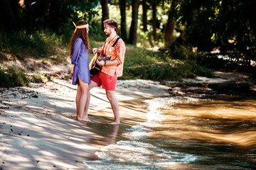 Fototapeta premium Beautiful young couple in love in hippie style with the guitar resting on the beach in summer. A man with his girlfriend talk on the shore alone