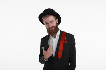 People, style and fashion concept. Waist up shot of fashionable confident bearded young European man wearing trendy hat, jacket and red tie on his shoulder, looking at camera with serious expression