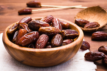 Sweet dried dates fruit in a wooden bowl and on the table.