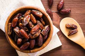Sweet dried dates fruit in a wooden bowl and in the spoon. Top view