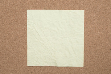 yellow creased paper note on cork background