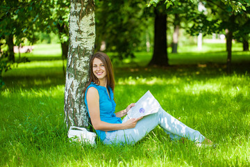 Happy brunette woman reading a womens magazine sitting on the green grass