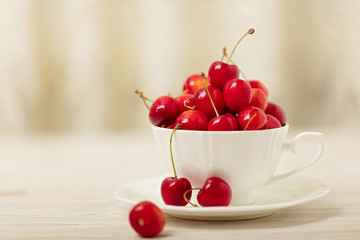 Cherries in a white cup on a light wooden background.