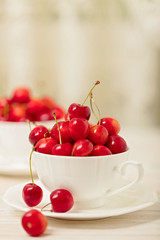 Cherries in a white cup on a light wooden background.