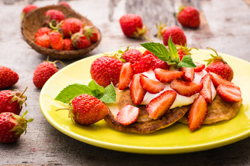 Pancakes with yogurt, sliced strawberries and mint leaves on a plate