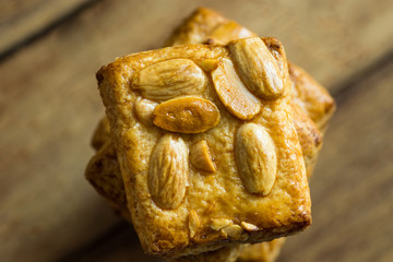 High stack of homemade almond Christmas cookies on plank wood background, top view, copy space, holiday baking, desserts