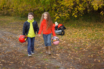 Little boy and girl with helmets in their hands walking along a rural road, holding hands. Autumn romantic date