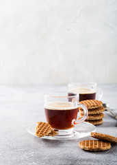 Glass cups of coffee with mini stroopwafel, syrupwaffles cookies on light gray background with copy space.