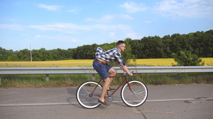 Obraz premium Young handsome man riding at vintage bicycle in the country road. Sporty guy cycling at the track. Male cyclist riding fixed gear bike at highway. Healthy active lifestyle Close up