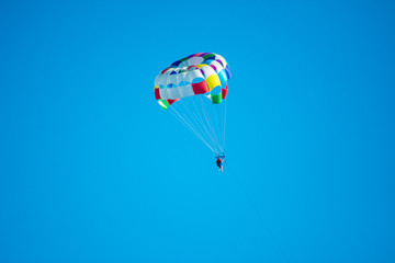 Fototapeta na wymiar Parasailor on multi-colored parachute flying in blue clear sky, sunny weather, inspirational, summer, vacations, freedom
