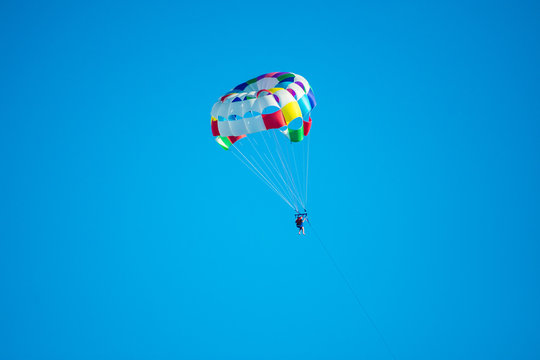 Parasailor on multi-colored parachute flying in blue clear sky, sunny weather, inspirational, summer, vacations, freedom