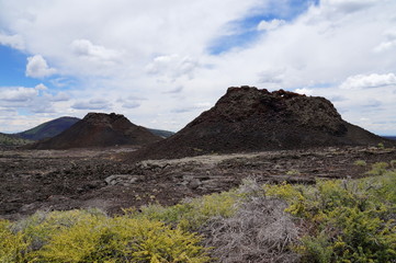 Two spatter cones and one cinder cone rising above a landscape of black volcanic basalt rock from eruptions along the Great Volcanic Rift Zone, a line of cones and lava vents. Craters of the Moon, USA