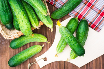 Fresh cucumbers on the cutting board and in a basket on a wooden table. Top view