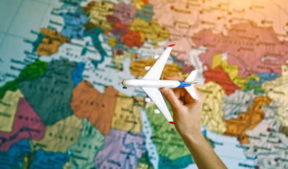 hand with toy model of airplane on world map background