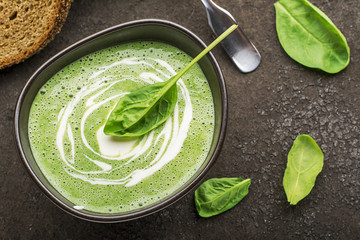 Homemade spinach soup puree in a dark bowl on a dark background with grain bread. Top View.