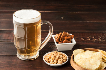 glass of cold frothy lager beer and peanuts plate on wooden table