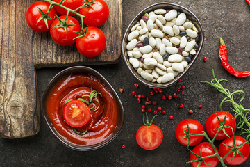 Dark ceramic bowl with tomato sauce, Assorted legumes, fresh vegetables, herbs, pepper on a dark background. Top View