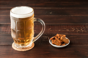 glass of cold frothy lager beer and plate of snacks on wooden table