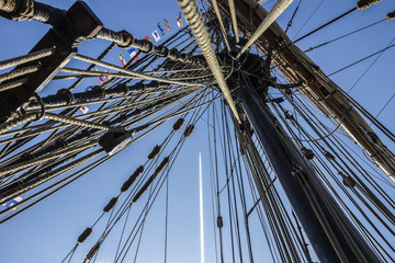 Fototapeta premium Nautical part of a yacht or a big old sailing ship with cords, rigging, sail, masts, knots, signal flags in front of a blue sky