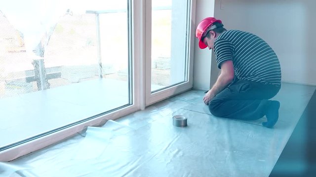 construction worker lay polyethylene film on floor.