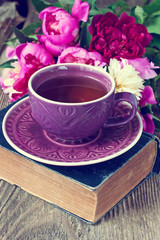 Tea cup and peonies on wooden table.