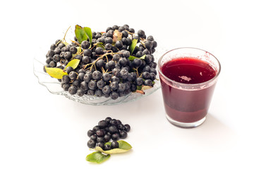 Fresh juice of black chokeberry (Aronia melanocarpa) in glass and beries in pot, isolated on white background