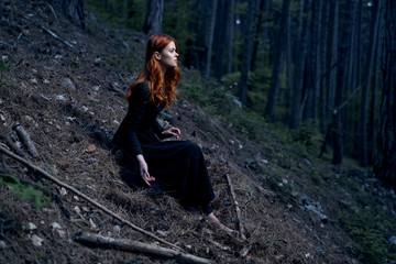 Naklejka na ściany i meble Beautiful young woman in a long dress is sitting in the woods
