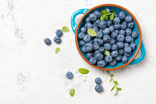 Fresh ripe blueberries with leaves in a bowl on a stone table, top view with copy space