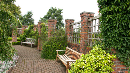 Benches in a walled garden with monoblock path and red brick pillars