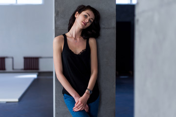 Smiling skinny female model standing at the wall wearing casual clothes