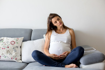 Young pregnant woman, sitting on couch in living room