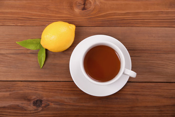 Cup of tea and lemon with leaves on a wooden background