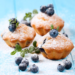 Homemade baked muffin with blueberries, fresh berries, mint, powdered sugar on blue wooden background. Top view.