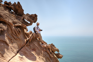 Nature photographer standing on edge of cliff above the sea.