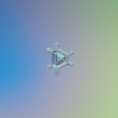 Real snowflake macro photo: small triangular snow crystal with six short, simple arms and glossy relief center with straight ridges. Snowflake glittering on smooth blue - green gradient background.