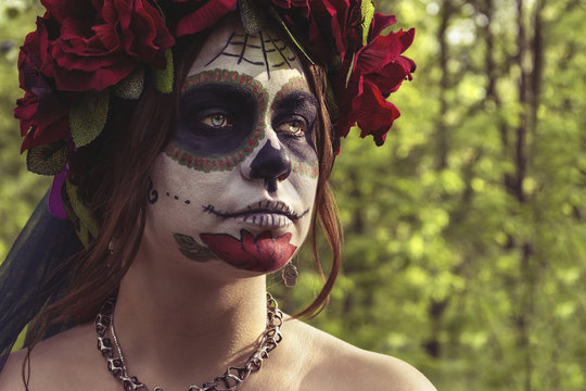 Beautiful woman  in makeup traditional Mexican Calavera skull Katrina in the autumn forest, in a wreath of red flowers. Day of the dead. Halloween celebration.