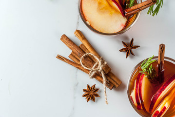 Fototapeta premium Christmas, Thanksgiving drinks. Autumn, winter cocktail grog, hot sangria, mulled wine - apple, rosemary, cinnamon, anise. On white marble table. With cones, rosemary. Copy space top view