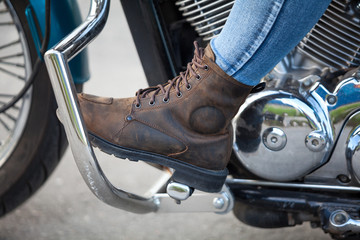 Side view at female foot with protective boot on the stands of chopper motorbike, close up