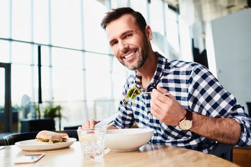 Smiling middle-aged man looking at camera while eating lunch in bright modern restaurant