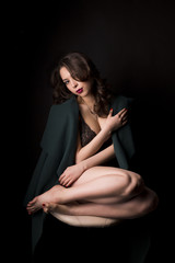 Pretty young woman in lace lingerie and green coat at studio