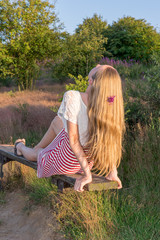 ein blondes Mädchen auf einer Parkbank  hängt Ihre langen Haare nach hinten in die Abendsonne