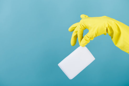 hand  in yellow glove holding sponge on blue background. cleaning